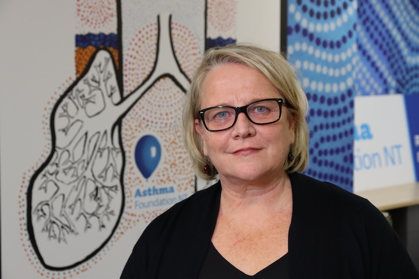 A woman smiling at the camera and standing in front of a banner featuring a large drawing of lungs.