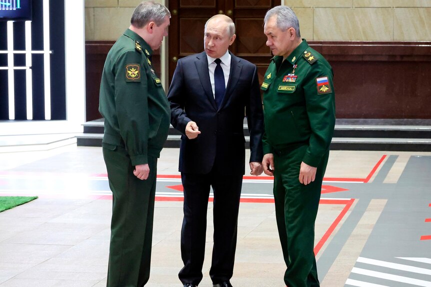 Putin stands with two men in green military uniforms.