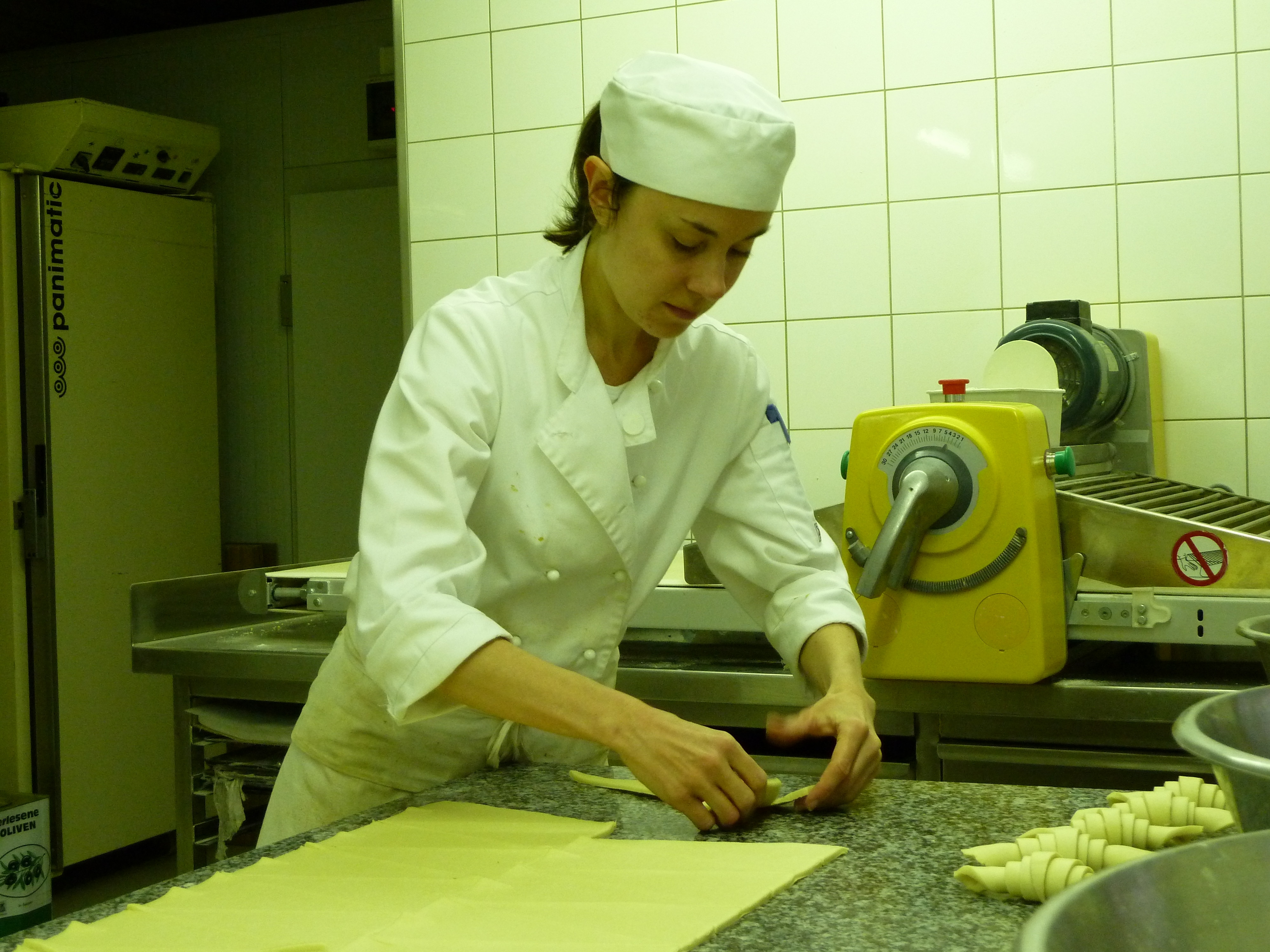 A young woman in chef jacket and hat working on pastry