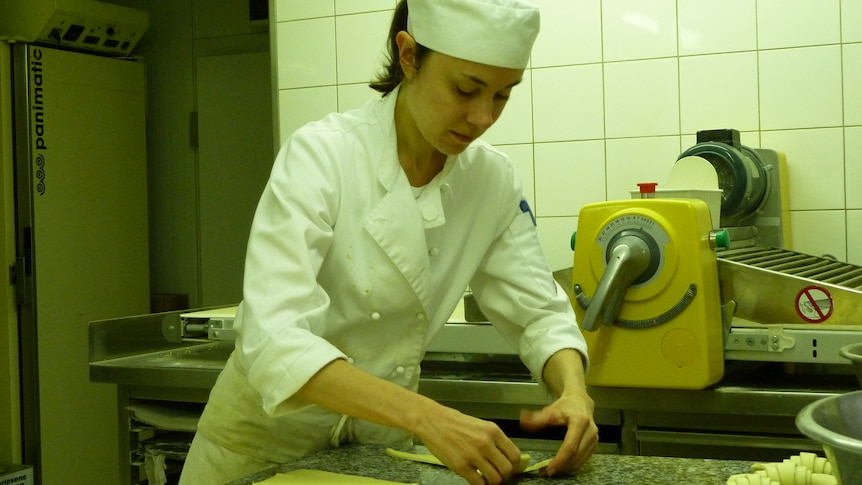 A young woman in chef jacket and hat working on pastry