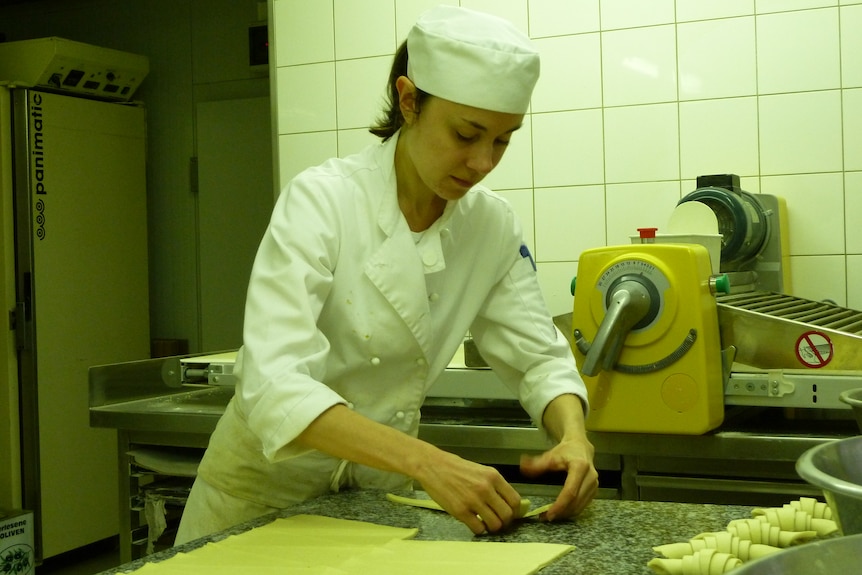A young woman in chef jacket and hat working on pastry