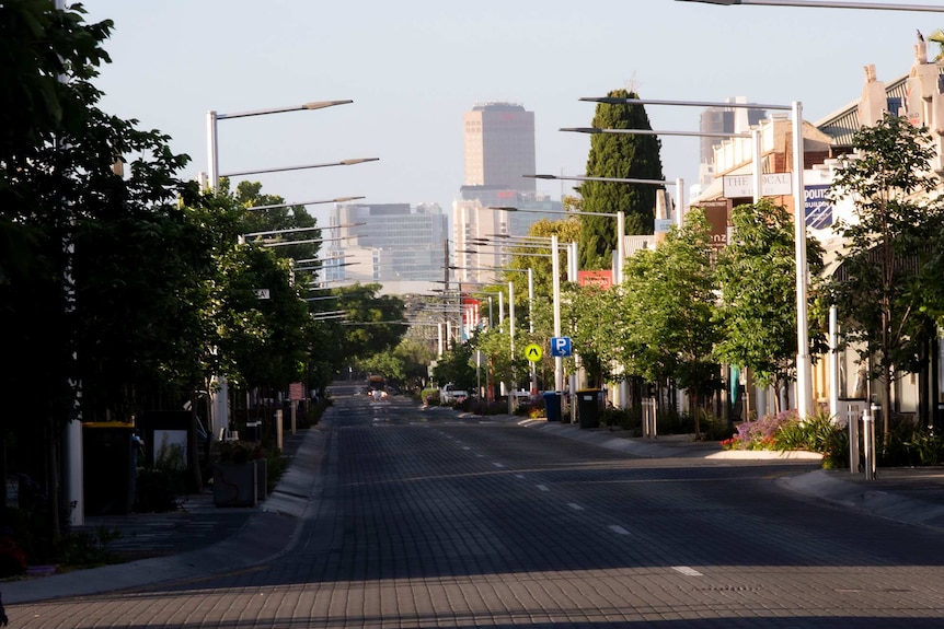 An empty shop-lined street with skycrapers in the background.