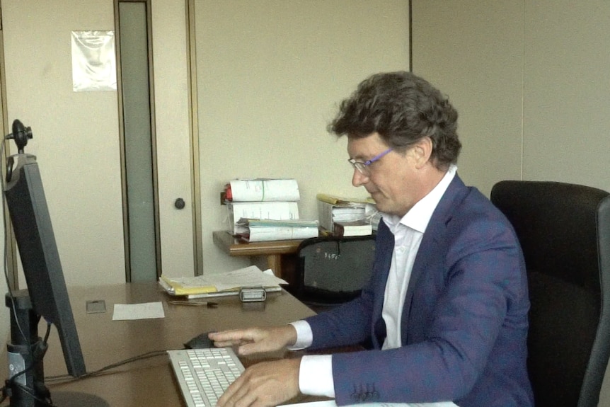 Stefano Castellani, an Italian man with wavy hair and glasses, sits at his desk in a messy office