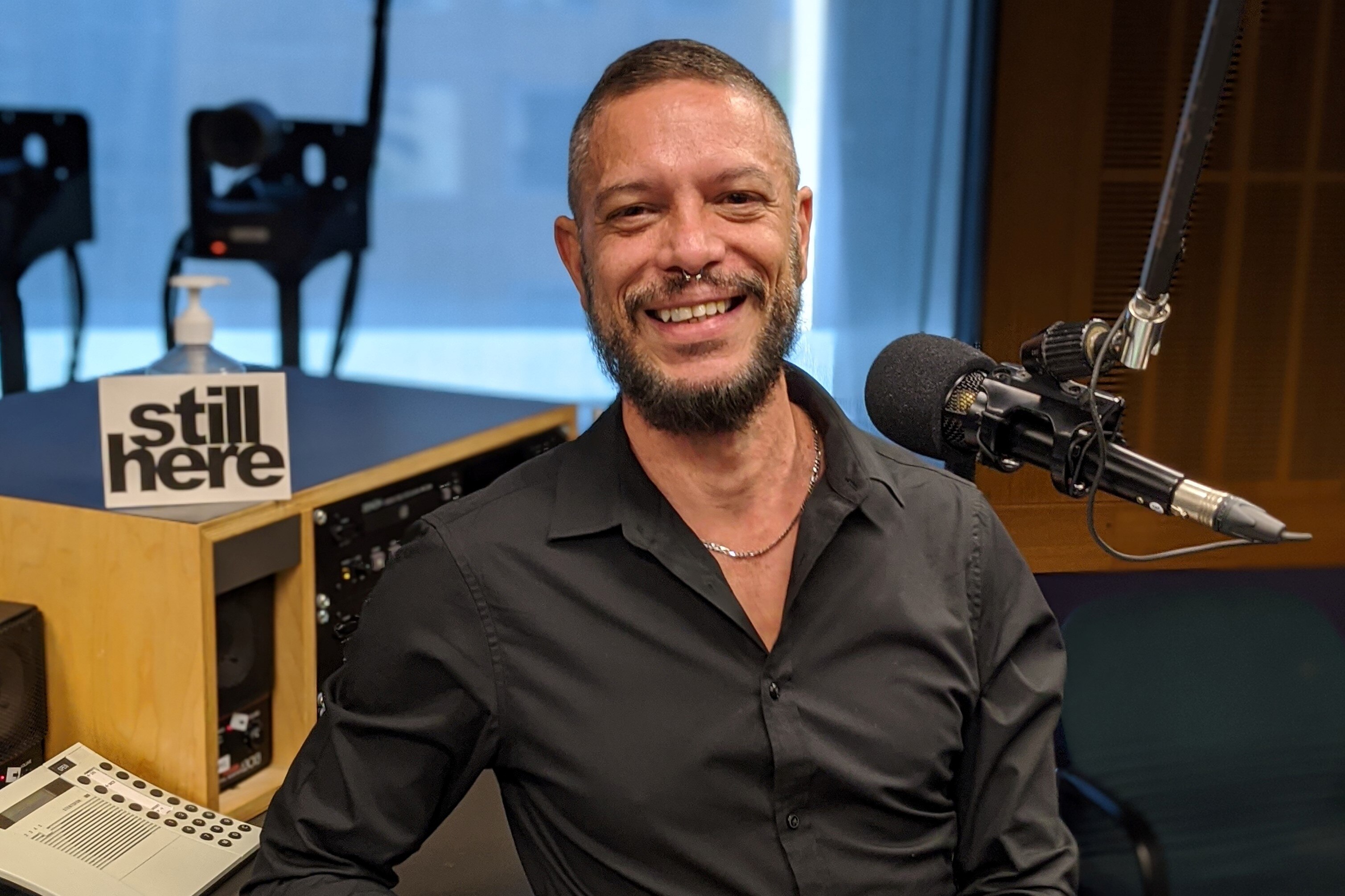An Aboriginal man in his late 40s in a black shirt sitting in a radio studio and smiling
