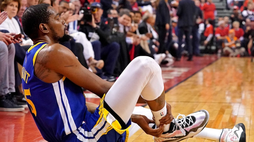 An injured basketballer sits on the court.