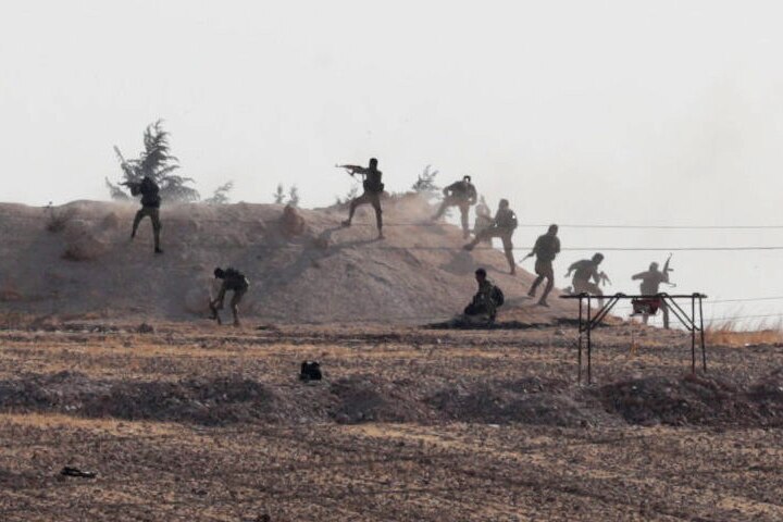 Turkey-backed Syrian rebel fighters are seen in action, climbing up on to a hill and firing guns. barbed wire in foreground