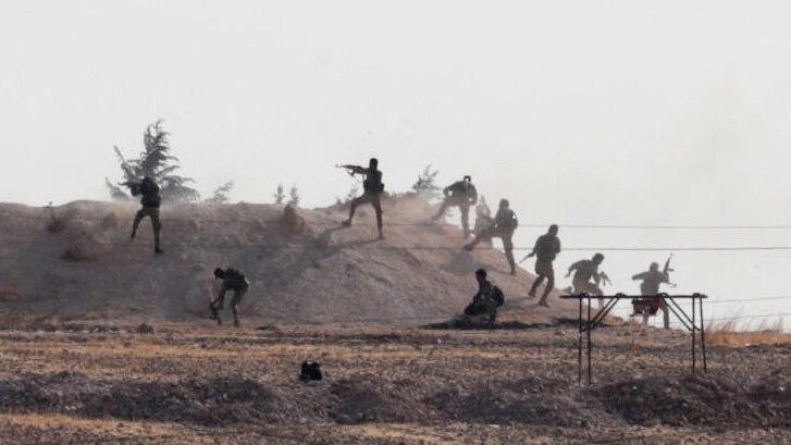 Turkey-backed Syrian rebel fighters are seen in action, climbing up on to a hill and firing guns. barbed wire in foreground