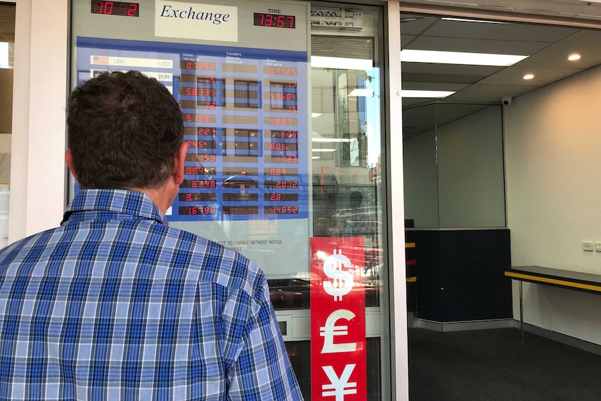Man looks at foreign exchange rates in window display.