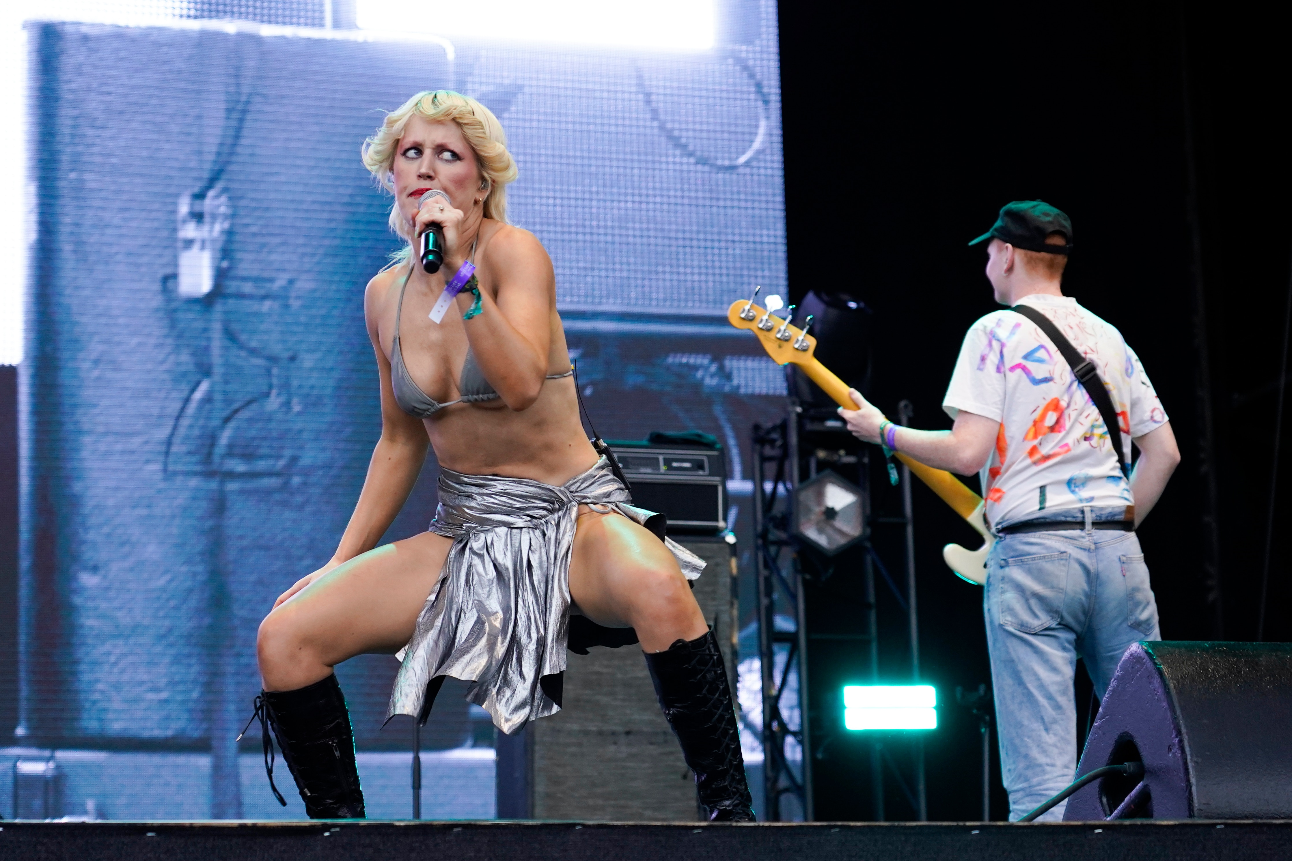 Una cantante con sujetador plateado y falda está en el escenario y sostiene un micrófono.