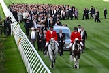 horses lead a hearse down the Flemington racetrack followed by mourners