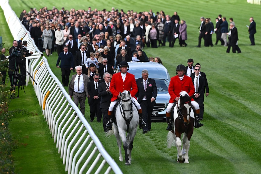 horses lead a hearse down the Flemington racetrack followed by mourners