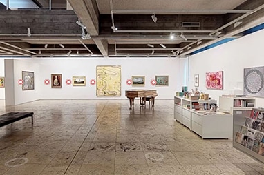 The interior of an art gallery, with paintings on the wall, a grand piano and a small gallery shop.