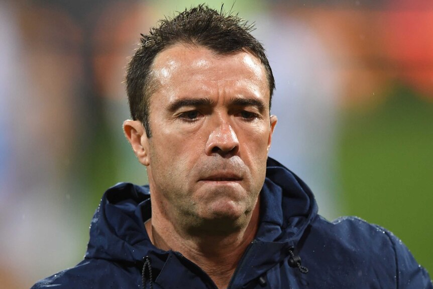 A close up shot of Chris Scott in a navy blue jacket with a grim expression.