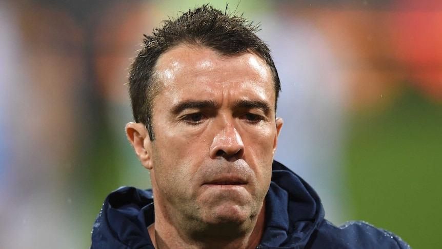 A close up shot of Chris Scott in a navy blue jacket with a grim expression.