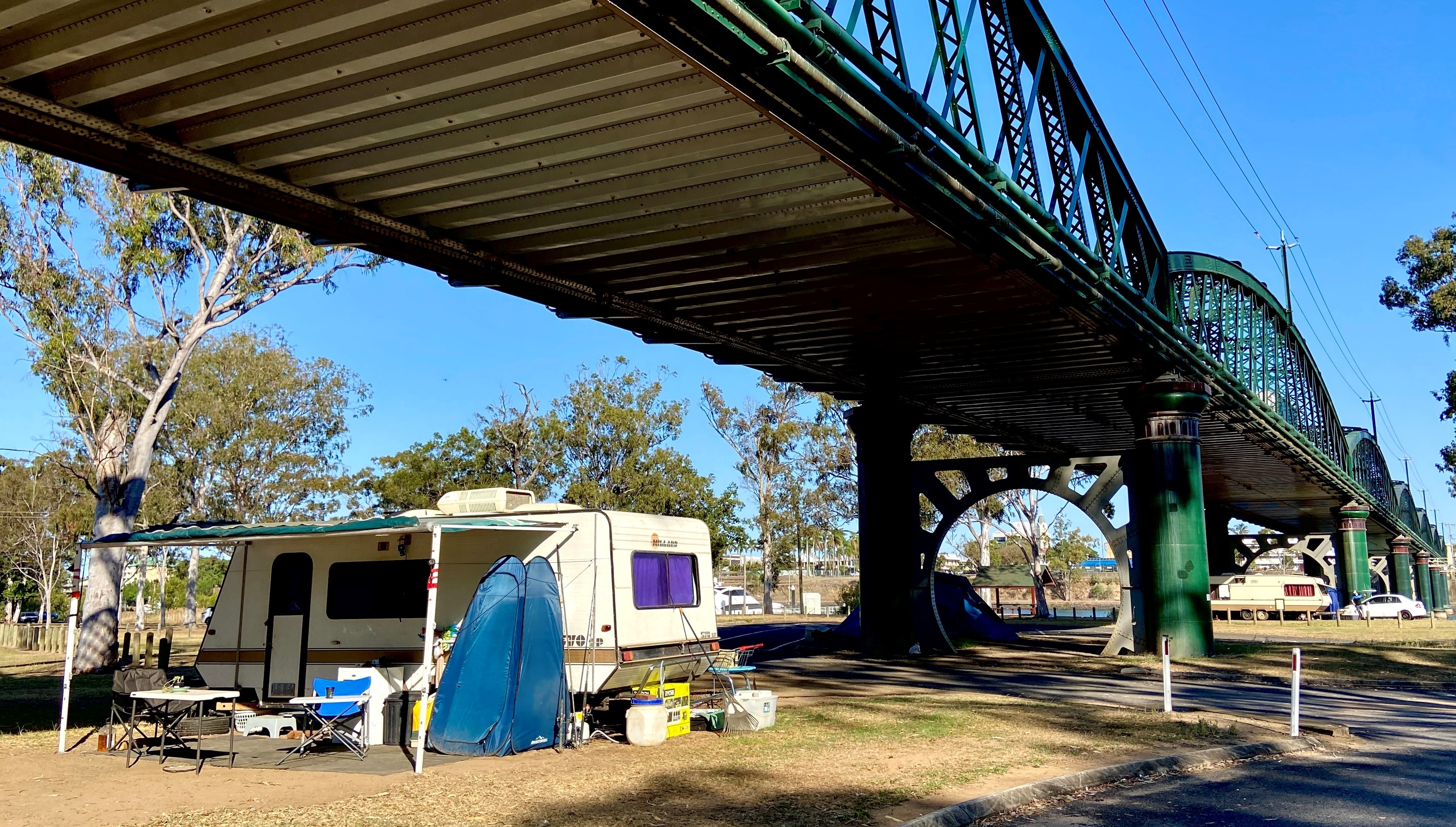 Tens set up in a park beneath a bridge.