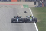 Two F1 cars driving down the main straight, touching their wheels with some debris flying off one of the cars.