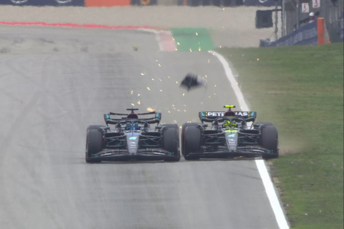 Two F1 cars driving down the main straight, touching their wheels with some debris flying off one of the cars.