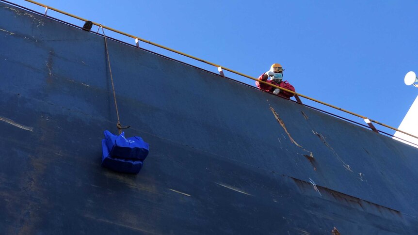 A man leans over a ship where a shopping bag is attached to a rope