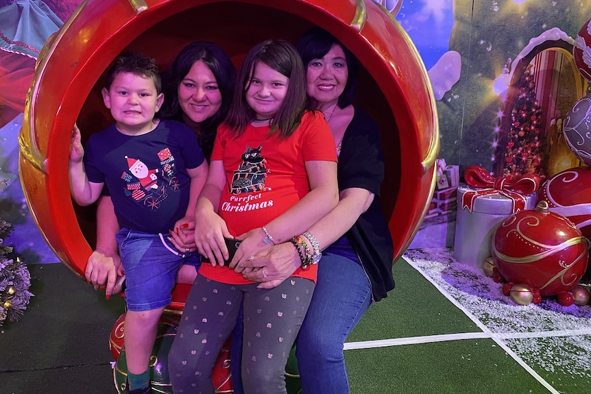 Carmen Garcia, her children Cooper and Ashlee and their Lola Aida sit in a Christmas bauble decoration smiling.