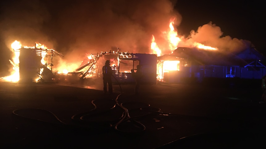 A building on fire at night with the silhouette of a firefighter and flash of blue lights.