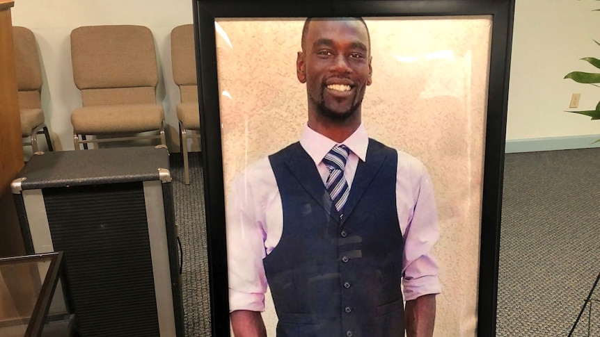 A framed photograph of a young, smiling black man dressed in a grey suit vest, tie and white shirt with the sleeves rolled up.