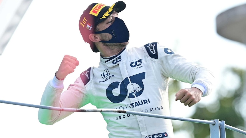 French F1 driver Pierre Gasly punches the air while wearing a black cap and mask.