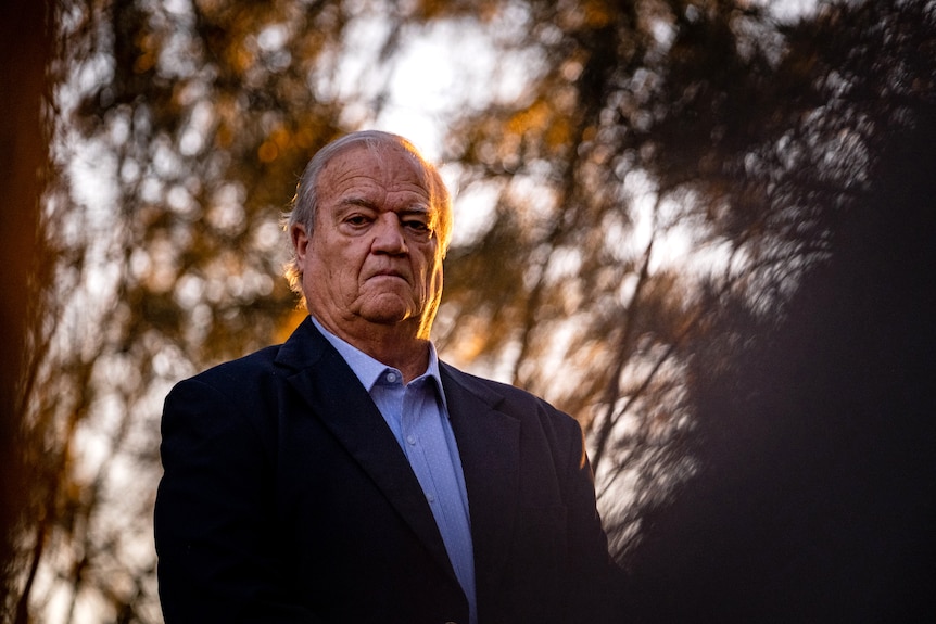 Mr Terrey stands outdoors, partly in shadow, gold sunset light on his face. Behind him are the shadows of tangled tree branches.