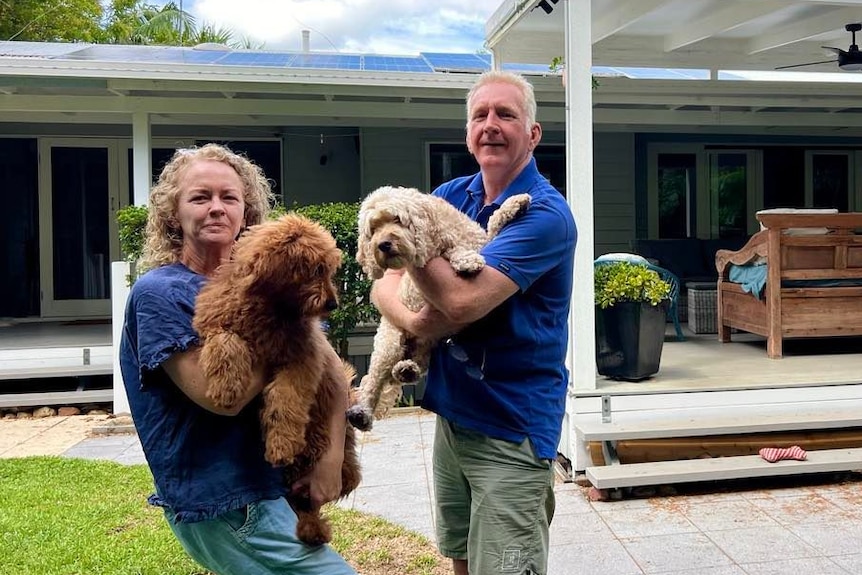 Woman and man holding a groodle and spoodle dog outside their home