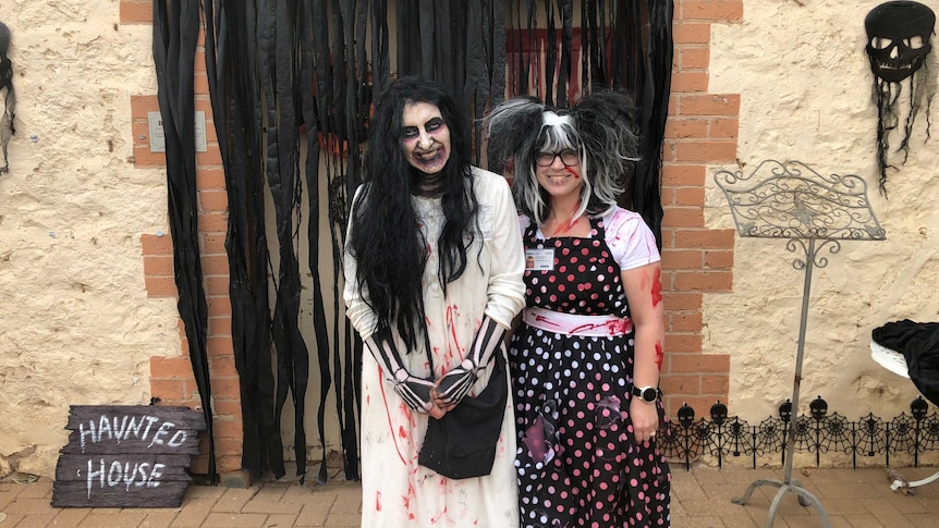 CJ Vogt and Emma White in Halloween costumes and facepaint outside an old bakery decorated as a Haunted House.