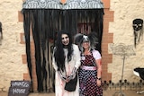 CJ Vogt and Emma White in Halloween costumes and facepaint outside an old bakery decorated as a Haunted House.