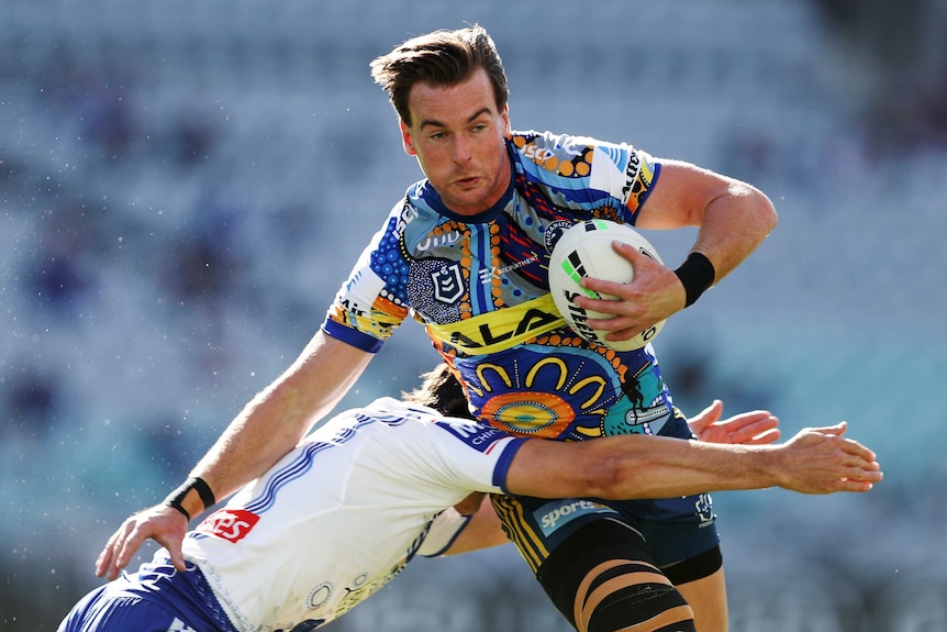 A Parramatta Eels NRL player holds the ball with his left hand as he attempts to fend off a Canterbury tackler.