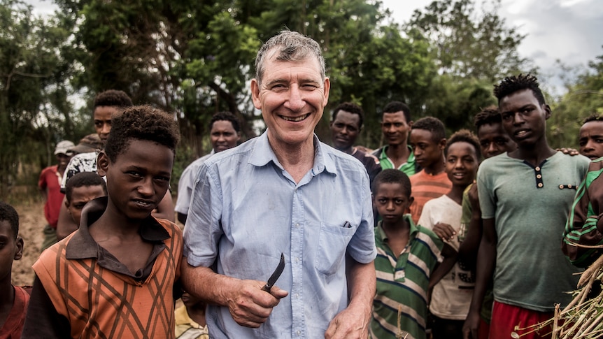 An older white man stands with a group of black men in a field