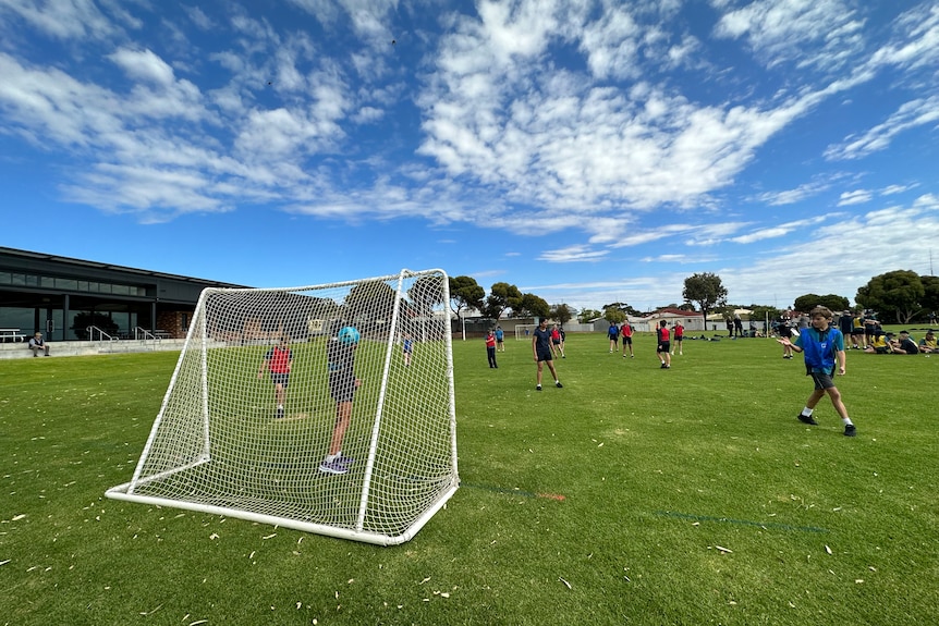 A small football goal net with kids playing and a blue sky in the background