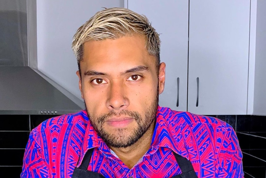 A young Pacific Island man with blonde hair wearing an island t shirt and a black apron
