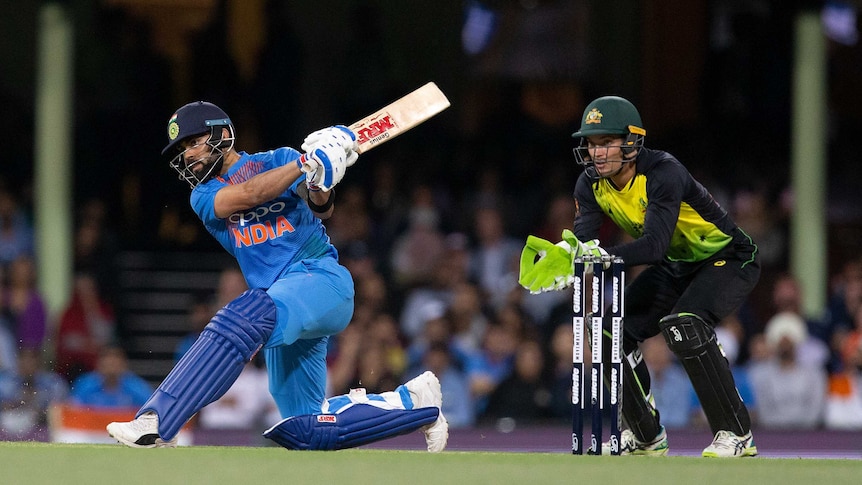 Virat Kohli sweeps at night time, while Australia wicketkeeper Alex Carey looks on.