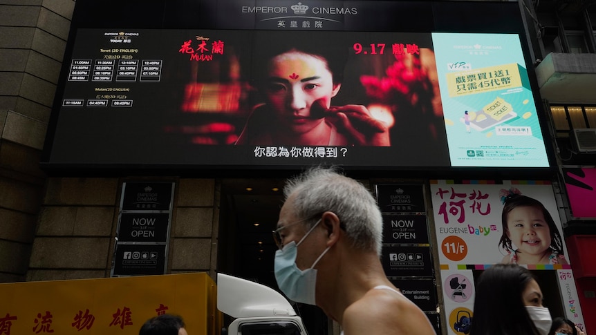 People walk past a huge TV screen showing movie listings in Hong Kong