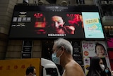 People walk past a huge TV screen showing movie listings in Hong Kong