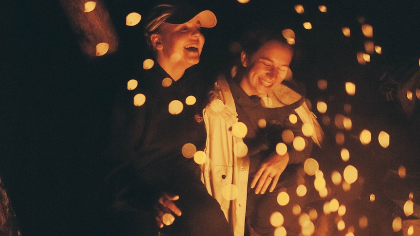 Two women laughing around a campfire
