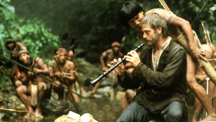 A man plays the oboe to a group of inquisitive tribesman