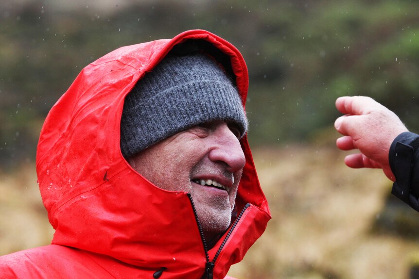 A man's face can be seen under a raincoast hood