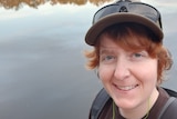 Woman wearing cap standing in front of a lake, for a story about challenges in seeking a hysterectomy.