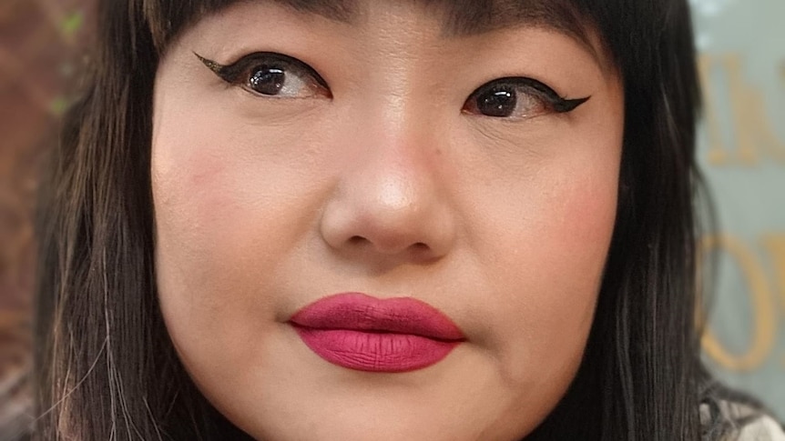 A woman with red lipstick, black winged eyeliner and black hair poses for the camera. 