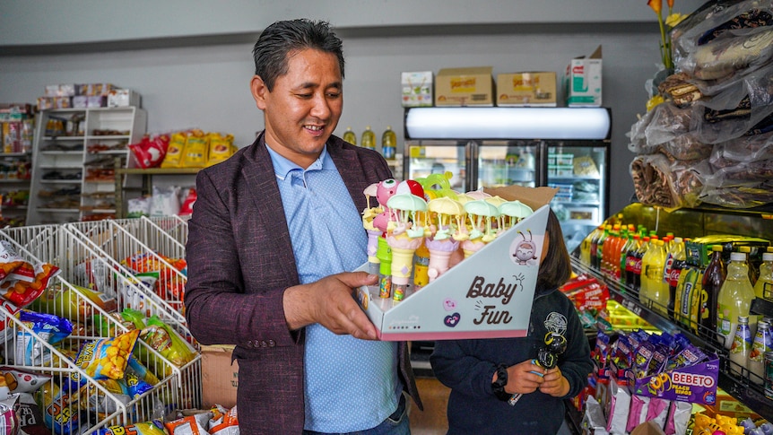 A man stands in a grocery store smiling, holding a box of baby toys.