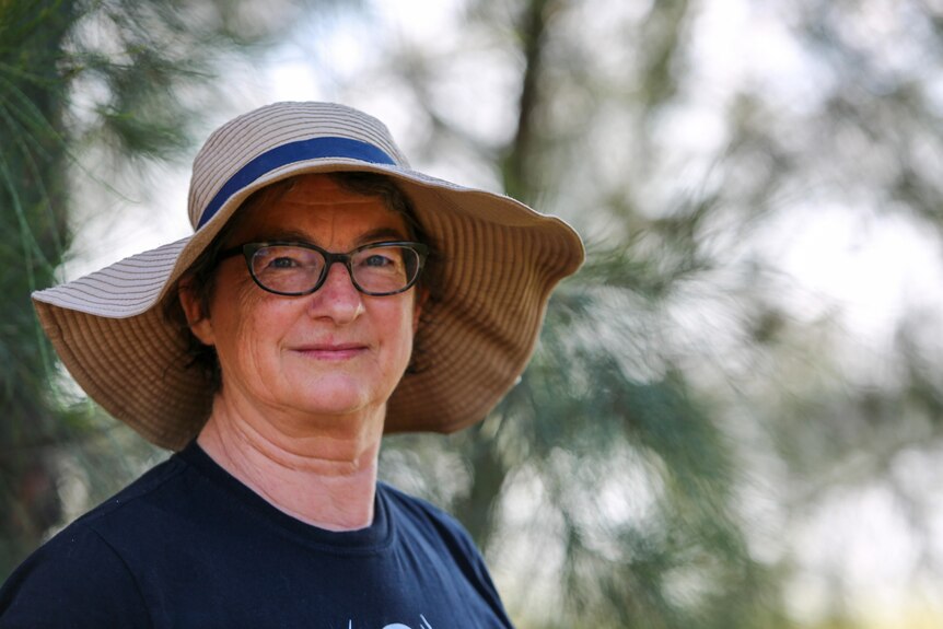 Diana Rice wearing a broad brimmed hat and navy shirt, standing in front of trees