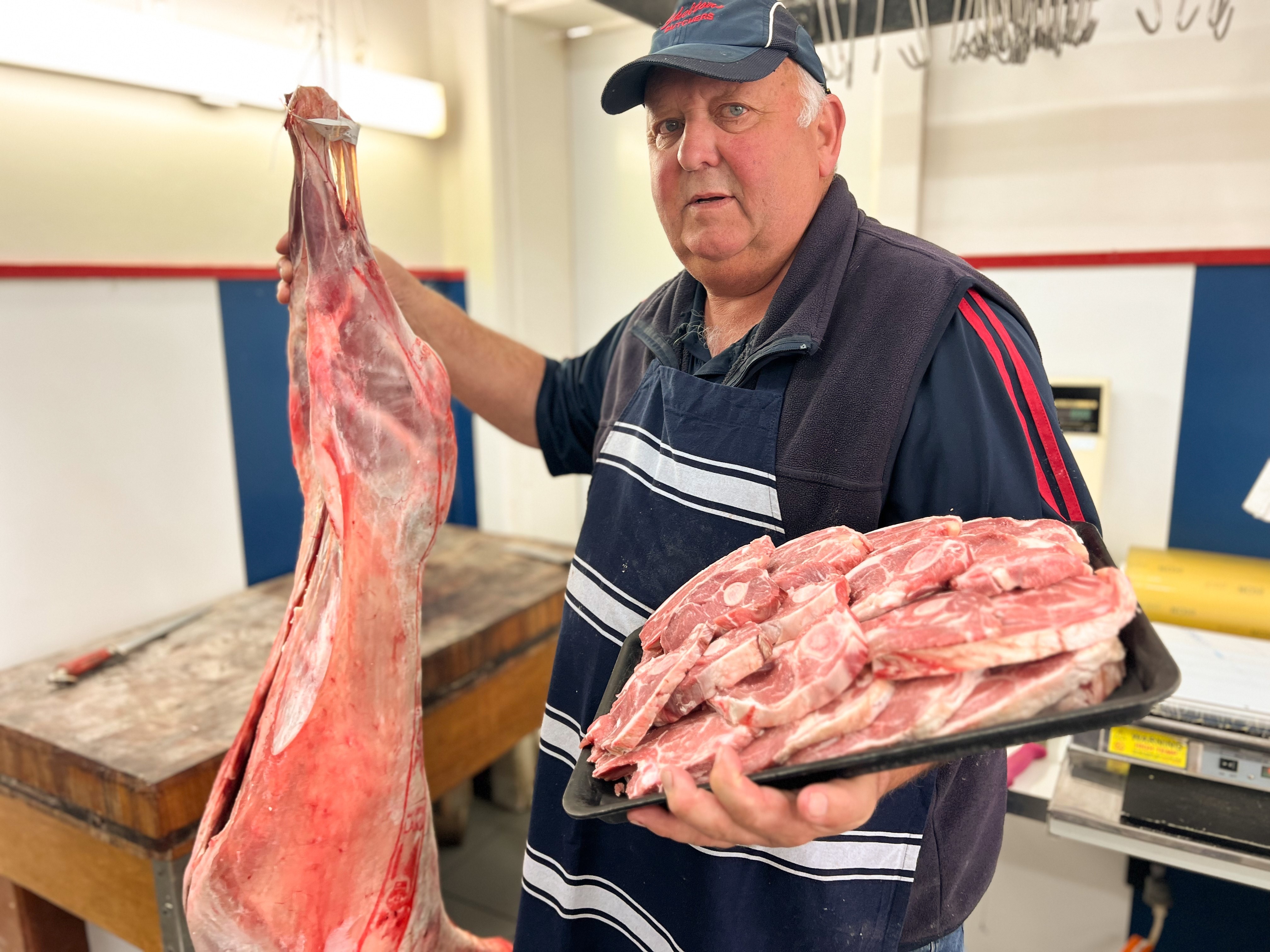 A male butcher holding a skinned lamb and lamb chops
