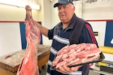 A male butcher holding a skinned lamb and lamb chops
