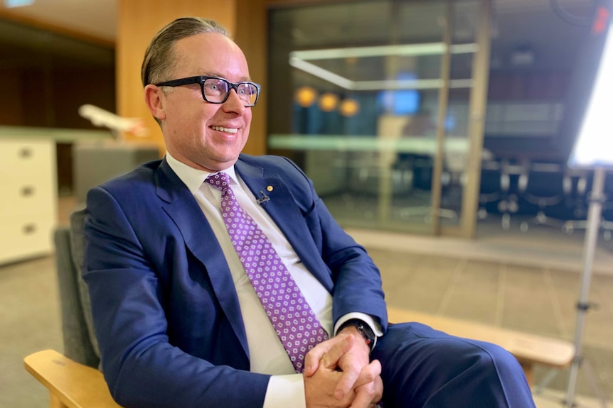 Qantas CEO Alan Joyce seated and smiling for a TV interview.