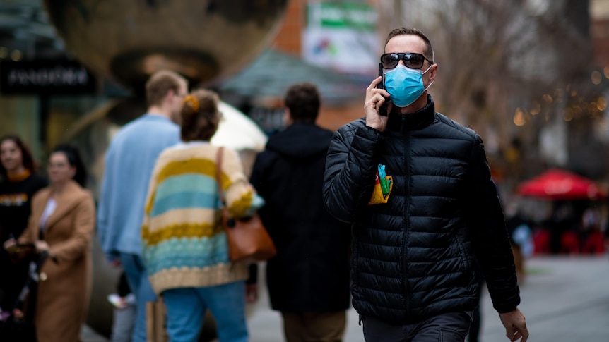 A man wearing a face mask and a black puffy jacket while speaking on a mobile phone