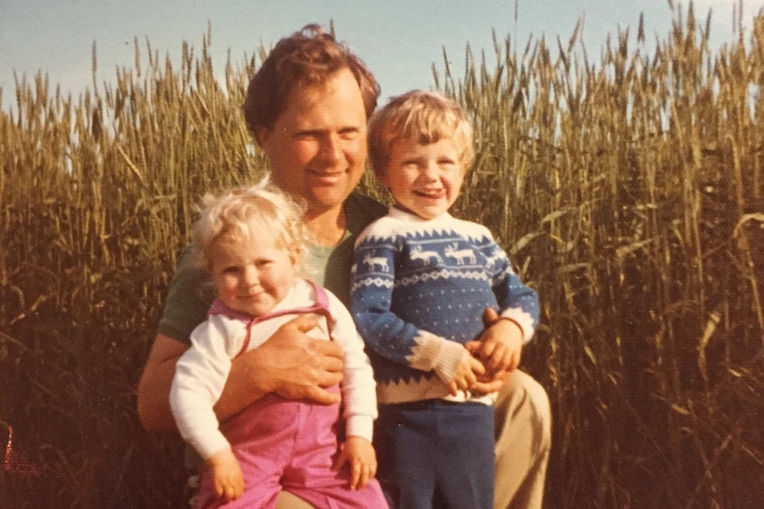 Man crouching in wheat field with daughter on his knee and son standing in front.