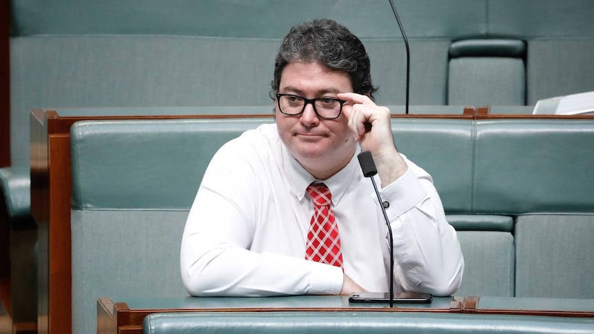 A dark-haired, bespectacled man wearing a crisp white shirt and a red tie sitting in federal Parliament.